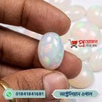 Close-up of an oval natural Australian White Opal gemstone displaying vivid green and red fire held between fingertips by Proyojonstore