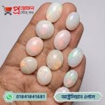 Multiple polished oval and round Australian White Opal gemstones with vivid multi-color fire flashes displayed on an open hand by Proyojonstore