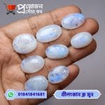 Array of eight smooth oval natural Srilankan Blue Moonstone gemstones with glowing blue sheen displayed on an open hand by Proyojonstore