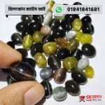 Fingertips holding a smooth dark brown-black natural Srilankan Cat's Eye gemstone displaying a distinct luminous ray above a pile of gems by Proyojonstore