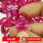 Fingertips holding a faceted oval natural pink Karu Ruby gemstone with subtle natural inclusions above loose stock by Proyojonstore