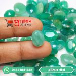 Hand holding a faceted light green oval Brazilian Emerald stone above a pile of green gemstones by Proyojonstore