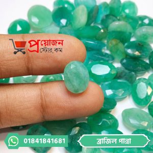 Hand holding a faceted light green oval Brazilian Emerald stone above a pile of green gemstones by Proyojonstore