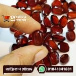 Close-up of a faceted oval deep reddish-brown natural African Gomed gemstone held between fingertips over loose gems by Proyojonstore