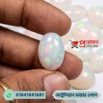 Macro view of a smooth oval white natural Australian Fire Opal gemstone displaying radiant green and red fire held between fingertips by Proyojonstore