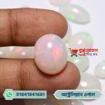 Fingertips holding a smooth round-oval natural Australian White Opal gemstone with bright reddish-pink fire reflections by Proyojonstore