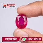 Close-up of a sparkling transparent oval faceted bright red Bangkok Ruby gemstone held between fingertips by Proyojonstore