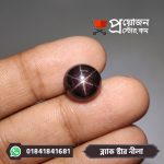 Macro close-up of a natural polished Black Star Sapphire cabochon with a sharp 6-ray star held between fingertips by Proyojonstore