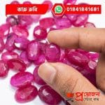 Macro view of an oval faceted pink-red natural Karu Ruby gemstone held between fingers above loose stones by Proyojonstore