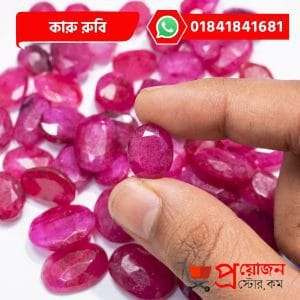 Macro view of an oval faceted pink-red natural Karu Ruby gemstone held between fingers above loose stones by Proyojonstore