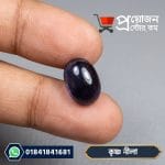 Smooth polished dark blue Krishno Nila sapphire gemstone resting on a finger
