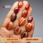 Multiple polished oval and teardrop shaped natural Yemeni Akik gemstones arranged on an open hand by Proyojonstore