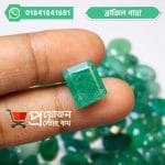 Fingertips holding a vibrant green rectangular faceted Brazilian Emerald gemstone above loose gemstones by Proyojonstore