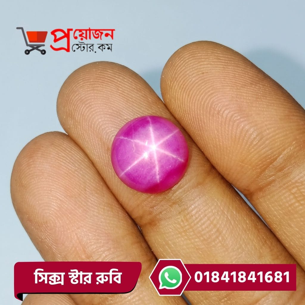 Macro close-up of a vibrant pinkish-red round natural Six Rays Star Ruby cabochon gemstone held between fingers by Proyojonstore