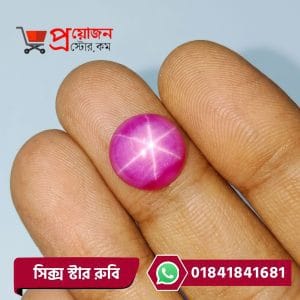Macro close-up of a vibrant pinkish-red round natural Six Rays Star Ruby cabochon gemstone held between fingers by Proyojonstore