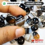 Hand holding a polished banded Solemani Akik gemstone above a pile of loose agate stones by Proyojonstore