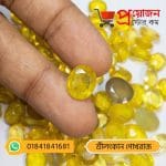 Close-up of a sparkling oval faceted golden-yellow Srilankan Yellow Sapphire gemstone held between fingertips over a batch of gems by Proyojonstore