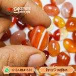 Finger holding a vibrant orange natural Yemeni Akik stone featuring a distinct white diagonal band by Proyojonstore