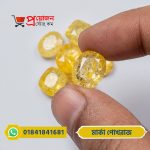 Hand holding a faceted oval Marka Yellow Sapphire gemstone above a pile of yellow gemstones by Proyojonstore