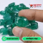 Close-up of a sparkling faceted oval green natural Colombian Emerald gemstone held between fingertips over loose gems by Proyojonstore