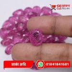 Fingertips holding a faceted oval natural pink Marka Ruby gemstone above a collection of stones by Proyojonstore
