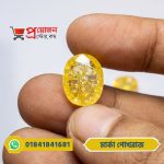 Close-up of a sparkling oval faceted natural Marka Yellow Sapphire gemstone held between fingertips by Proyojonstore